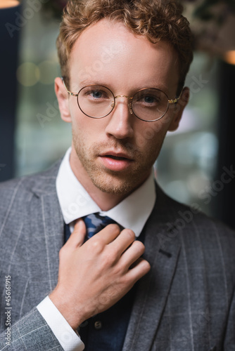 good-looking young businessman in formal wear and glasses adjusting tie in cafe
