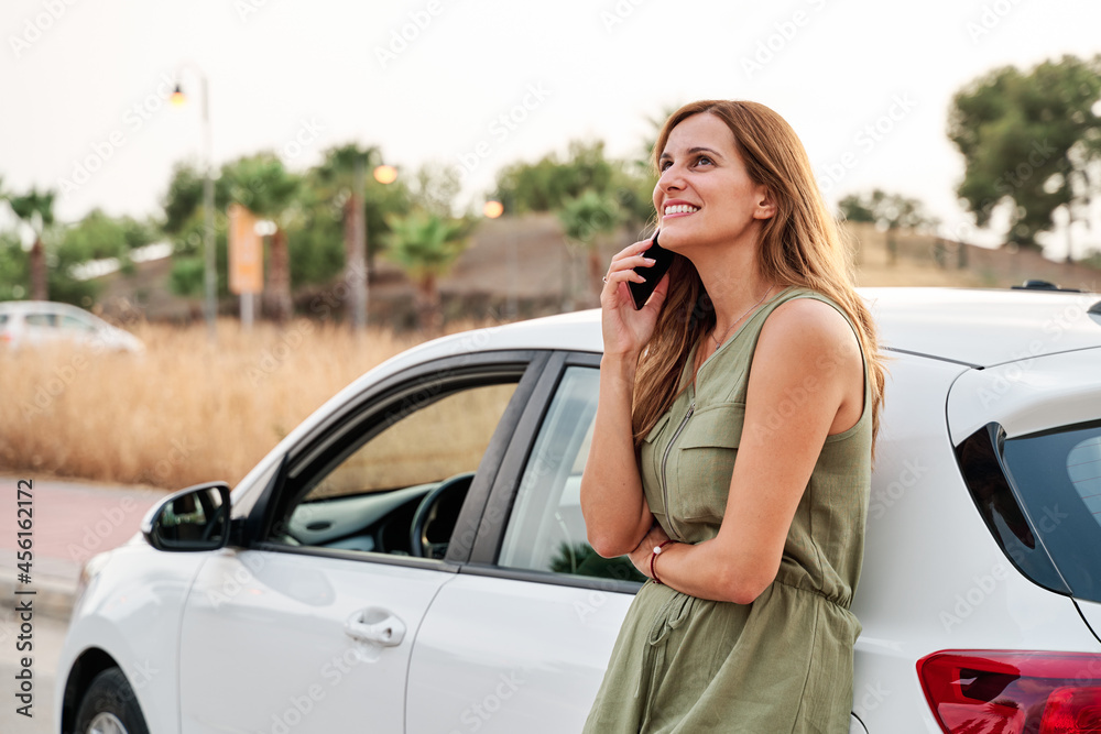 Young pretty woman standing leaning against her car while talking on her smartphone. Young pretty woman standing leaning against her car while talking on her smartphone.