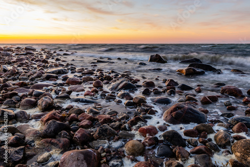 Beautiful golden sunset over the rocky sea. Waves are reaching to coast during sunset at Tahkuna, Hiiumaa, Estonia. Coastal rocks and motion of ripples at sundown