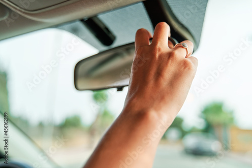 Close-up detail shot of an unrecognizable woman's hand adjusting the rearview mirror inside the car.