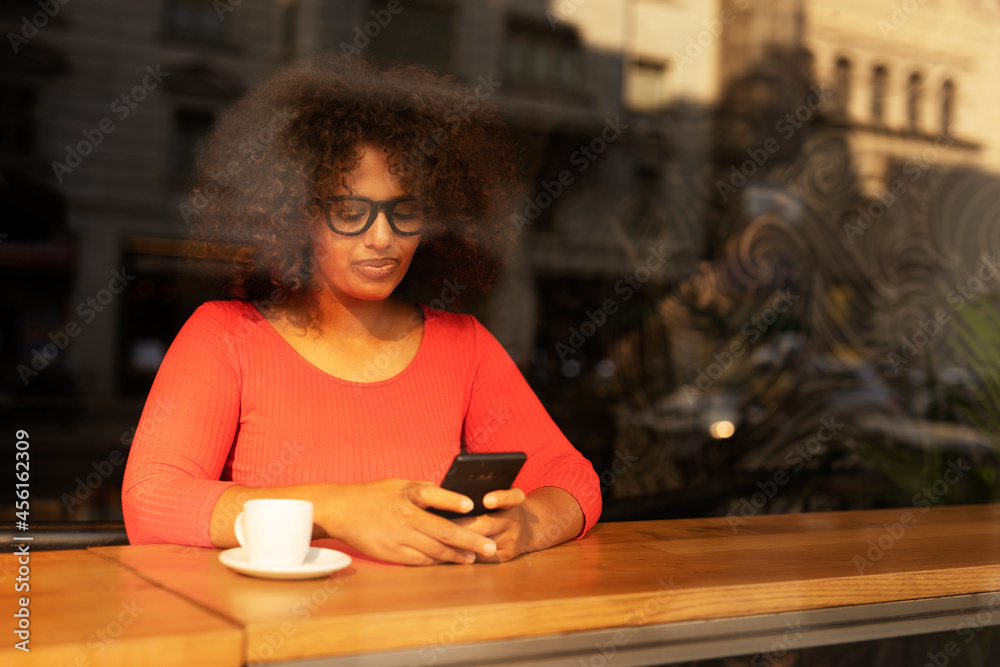 Young woman at cafe drinking coffee and using mobile phone. Beautiful African woman typing a message.