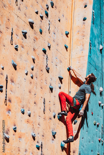 One Caucasian man professional rock climber workouts on climbing wall at training center in sunny day, outdoors. Concept of healthy lifestyle, power, strength, motion.