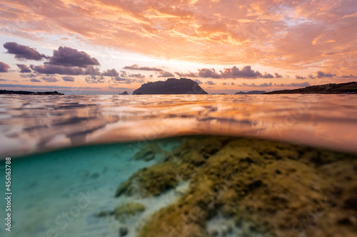 (Selective focus) Split shot, over under water surface. Defocused waves in the foreground with Tavolara Island on the surface during a dramatic sunrise. Porto Istana, Sardinia, Italy. © Travel Wild
