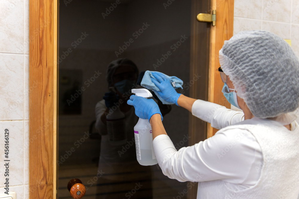 Fototapeta premium A woman in protective gloves and suit performing cleaning and disinfection in public sauna areas.Desinfection with antibacterial spray in hospital .