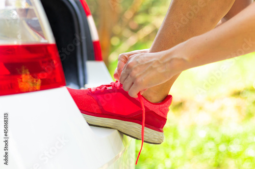 Women's hands in the forest near the car against the background of green trees on a bright summer sunny day tie the laces of sneakers. Selective focus