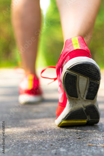 Women's legs in bright red sneakers while jogging in the park on the road on a summer sunny day. Selective focus