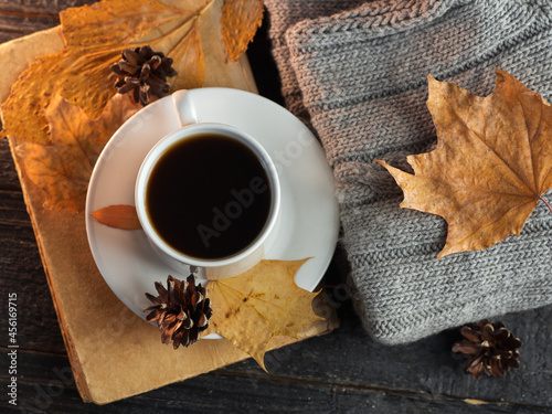 Top view of a cup of espresso coffee on a black wooden table, knitted warm autumn or winter clothes, an old book, dry leaves