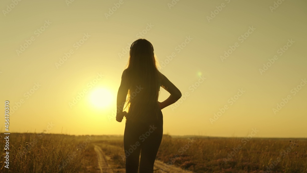 happy girl runs to meet her dream at sunset, doing sports jogging at dawn, listening to music in an active morning jog in rays of sun light, taking care of her health and being in shape, human figure