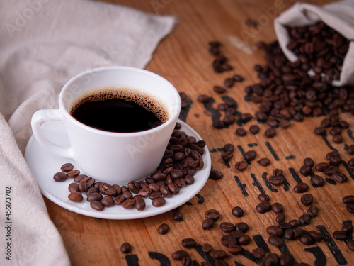 perspective of white coffee cup and organic coffee beans on vintage pine wood table top with side light shining on area. cafe concept on photography image.