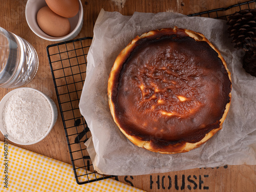 Basque burnt cheesecake placed on a black pastry rack with some ingredient, flour and eggs on vintage wood table. food concept on photography image.
