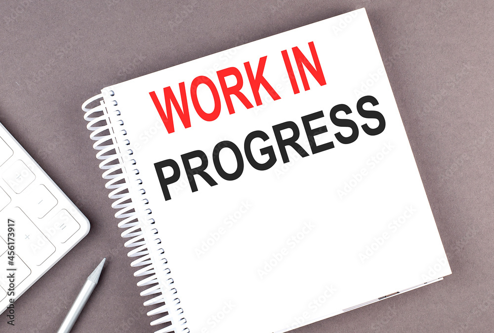 WORK IN PROGRESS text on the notebook with calculator and pen WORK IN PROGRESS text on the notebook with calculator and pen