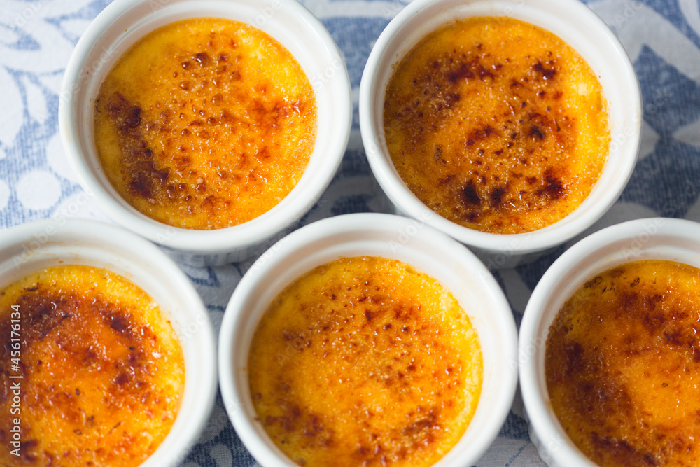 French dessert creme brulee with caramel crust in white baking molds on blue and white tablecloth French dessert creme brulee with caramel crust in white baking molds on blue and white tablecloth