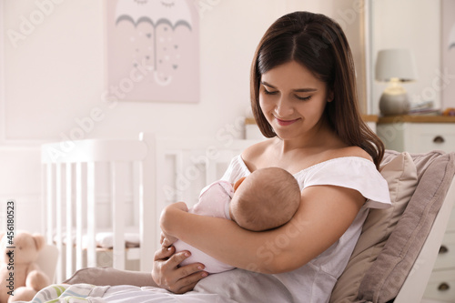 Happy young mother with her cute baby in armchair at home