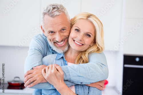 Photo of sweet pretty mature lovers dressed jeans shirt cuddling smiling indoors room home