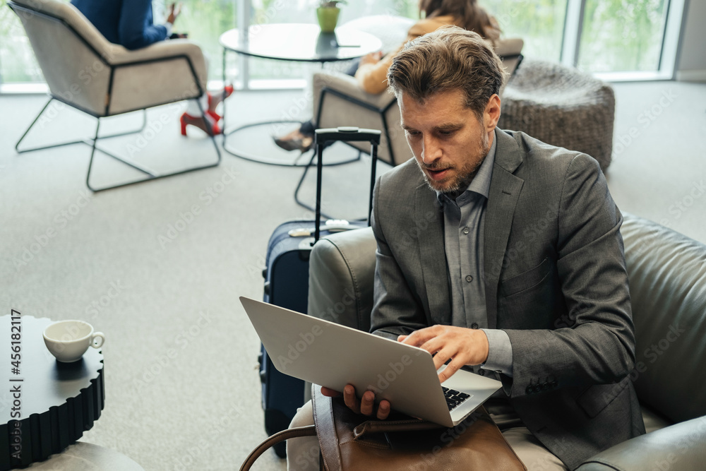 Businessman Using Laptop Computer while Waiting for his Flight in the  Business Lounge. Handsome business man sitting in armchair with carry on  luggage and working on laptop computer at airport. Stock-Foto