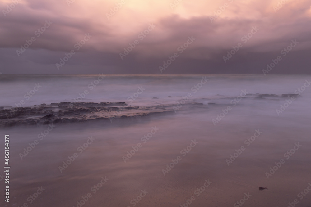 Long exposure photography at the edge of the sea. Dramatic sky during sunset on a stormy day.