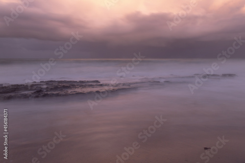 Long exposure photography at the edge of the sea. Dramatic sky during sunset on a stormy day.