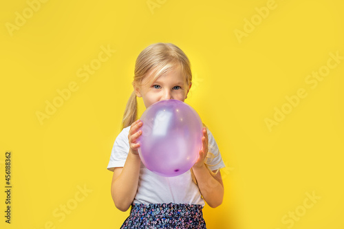 girl inflates a lilac balloon yellow background