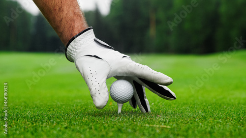 Male hands in a glove put a golf ball on the course