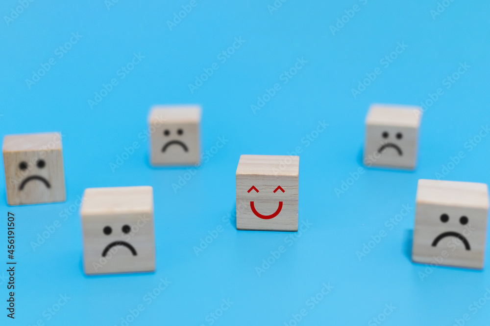 Happy and Unhappy emotion. happy smile face with sad face on wooden cube on blue background, positive think, social issues, customer satisfaction ,positive attitude, optimism and pessimism concept Happy and Unhappy emotion. happy smile face with sad face on wooden cube on blue background, positive think, social issues, customer satisfaction ,positive attitude, optimism and pessimism concept