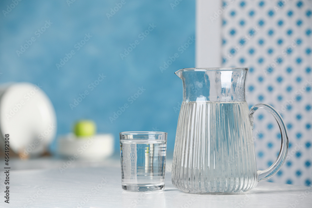 Jug and glass with water on white table indoors, space for text Jug and glass with water on white table indoors, space for text