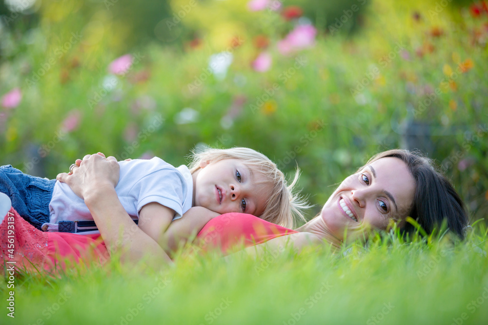 Mother and cute blond child, boy, lying in the grass, hugging and enjoying a tender moment between Mother and cute blond child, boy, lying in the grass, hugging and enjoying a tender moment between