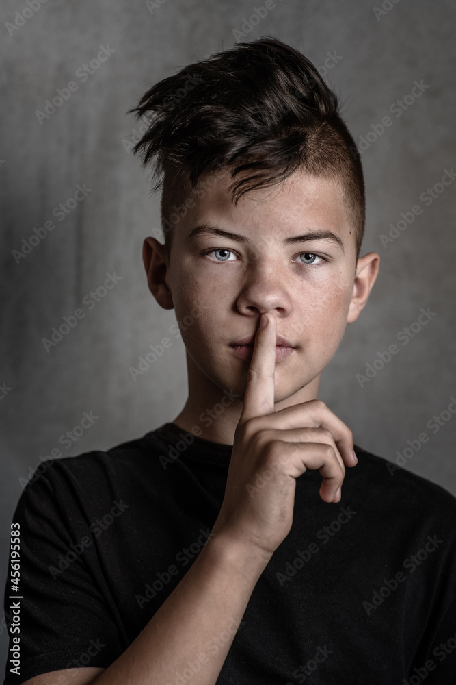 A teenage boy on a dark background pressed his index finger to his lips. Problems of adolescence in boys. No need to hush up the problems of puberty A teenage boy on a dark background pressed his index finger to his lips. Problems of adolescence in boys. No need to hush up the problems of puberty