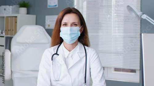 Portrait of beautiful young woman doctor sitting outdoors in medical mask and smiling. Coronavirus concept. Her cabinet on background photo