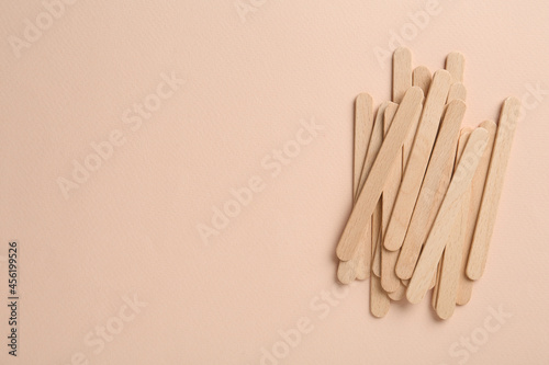 Wooden waxing spatulas on beige background, flat lay. Space for text