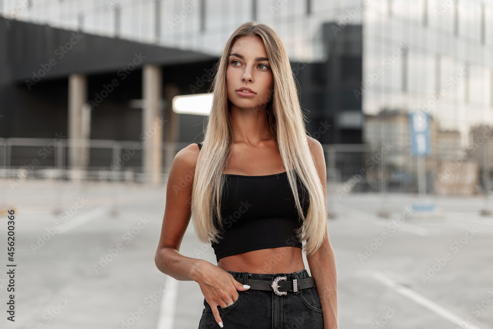 Fashion pretty young woman with a beautiful athletic body in a black t-shirt with jeans shorts posing in the city