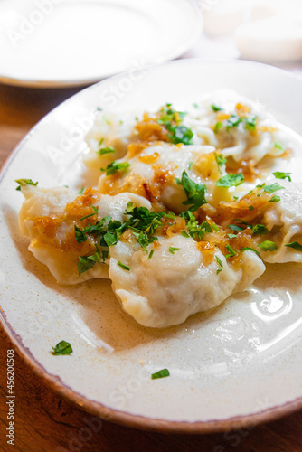 Delicious homemade polish dumplings stuffed with meats and caramelized onions on top served in white plate.