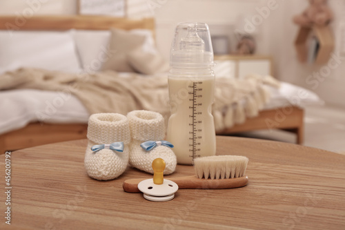 Slika na platnu Baby booties, pacifier, feeding bottle and brush on wooden table in bedroom