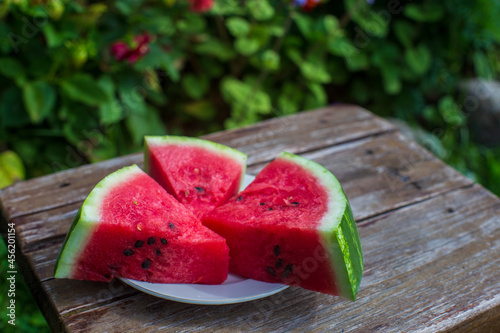 Slices of fresh red watermelon on a plate on a wooden surface in the garden against a background of flowers