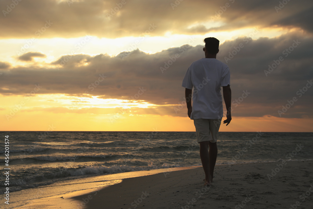 Man walking on sandy beach during sunset, back view