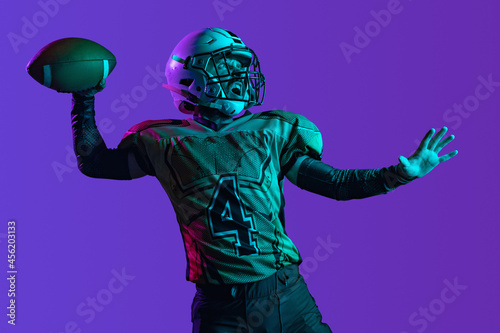 Throwing a ball. One professional american football player in special unofrm isolated over purple studio background. Campionship training photo