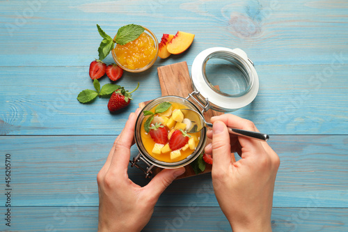 Fototapeta Naklejka Na Ścianę i Meble -  Woman eating delicious mango jelly with fresh fruits  at light blue wooden table, top view