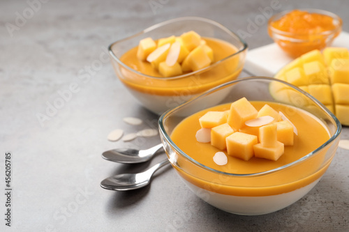 Delicious panna cotta with mango coulis and fresh fruit pieces on grey table. Space for text