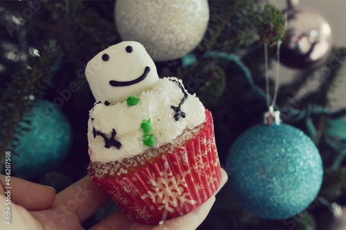 Homemade cupcake in the shape of a snowman against background of Christmas tree decorated by ornaments