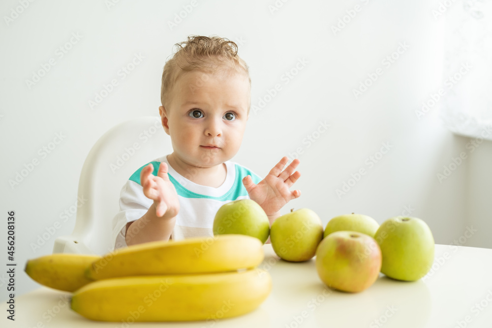 cute baby boy sitting sitting at the table in child chair eating apple on white kitchen. cute baby boy sitting sitting at the table in child chair eating apple on white kitchen.