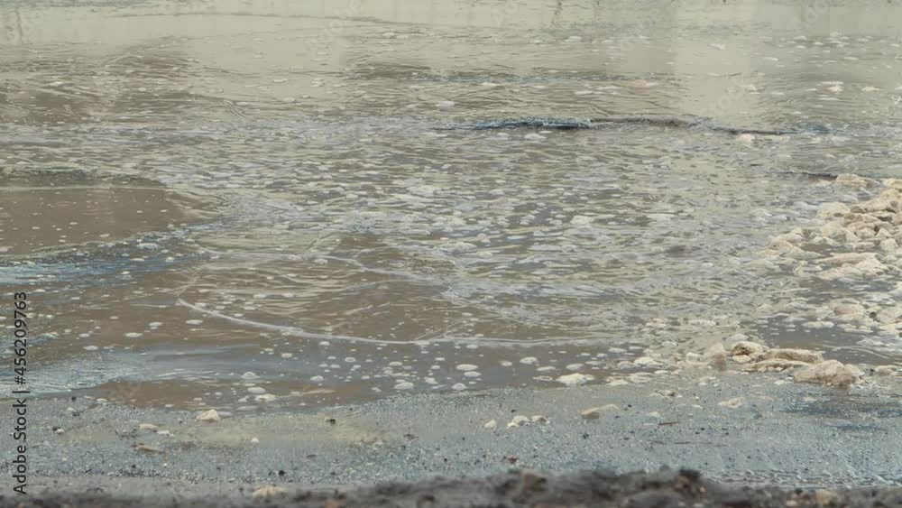 Large potholes after rain, badly damaged road infrastructure. Cars drive slowly along the road with pits and puddles. Asphalt in violation of technology. Taxpayer money is wasted. UHD 4K.