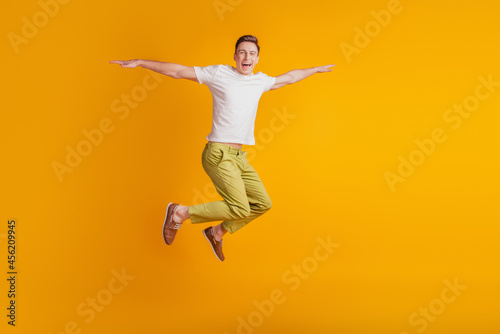 Portrait of athletic energetic active guy jump pretend airplane hands wings on yellow background © Tetiana