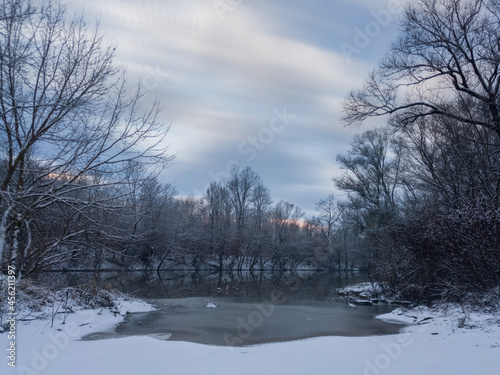 Calm snowy winter scene with river, snow covered riverbanks and naked trees