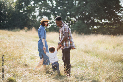 Happy multicultural family of having fun together on fresh air. Caucasian wife and african husband playing with their lovely son on summer field. Unity and values concept.