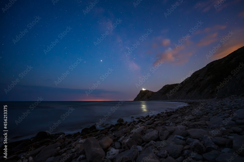 Amazing view with starry sky after sunset over rocky Black sea coast and cape Emine with the lighthouse, Bulgaria