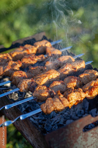 A lot of juicy meat kebabs in a row on the grill. Meat pieces strung on metal skewers on the grill at sunset. The process of cooking kebabs with a lot of smoke. Cooking in nature