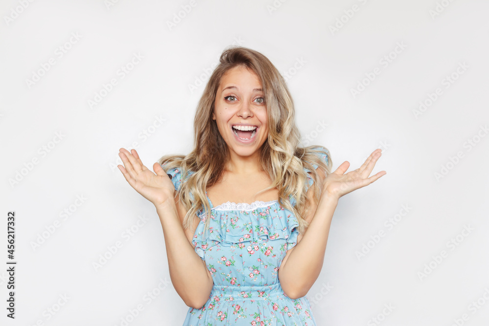 A young caucasian amazed blonde woman with wavy hair stands with her arms raised. A smiling happy girl is surprised and glad to hear the good news about something isolated on a white background A young caucasian amazed blonde woman with wavy hair stands with her arms raised. A smiling happy girl is surprised and glad to hear the good news about something isolated on a white background