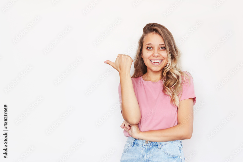 A young caucasian pretty charming blonde woman with wavy hair in a pink t-shirt points to a copy empty blank space for text or design with her finger presenting product isolated on a white background A young caucasian pretty charming blonde woman with wavy hair in a pink t-shirt points to a copy empty blank space for text or design with her finger presenting product isolated on a white background