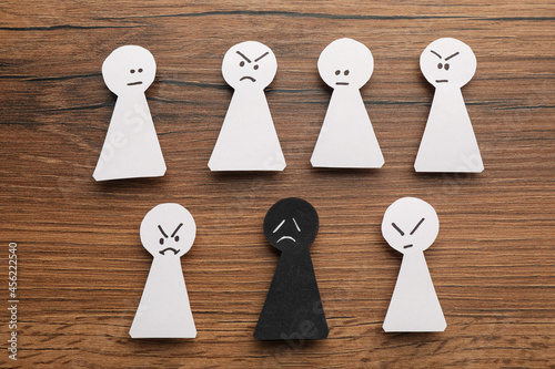 Flat lay composition with black and white paper figures on wooden table. Racism concept photo