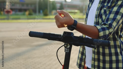 Unrecognizable tourist man take electric kick scooter or bike bicycle in sharing parking lot, smart watch application. Eco transportation. Smartwatch phone app for scooter