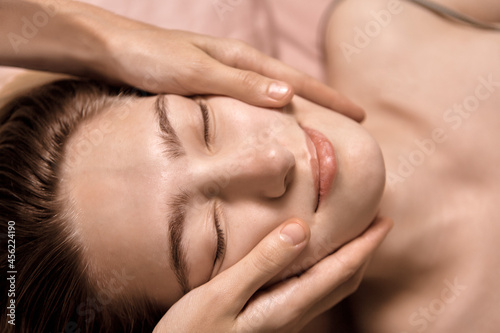 Young beautiful woman is getting a relaxing head and face massage in wellness center. Masseur doing massage the head of an young beautiful girl woman in the spa salon close up macro